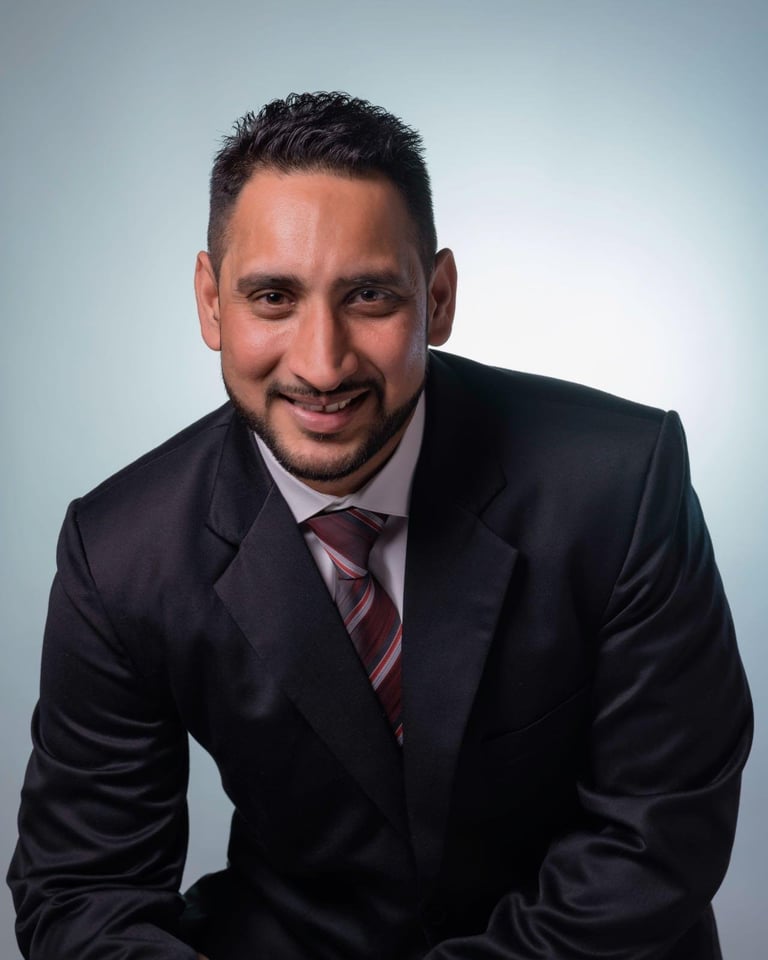 Professional headshot of a smiling man in a dark suit and striped tie against a light blue background